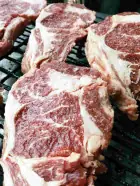 Thick-cut grilled beef steaks with visible marbling on a metal grill at Can Marti
