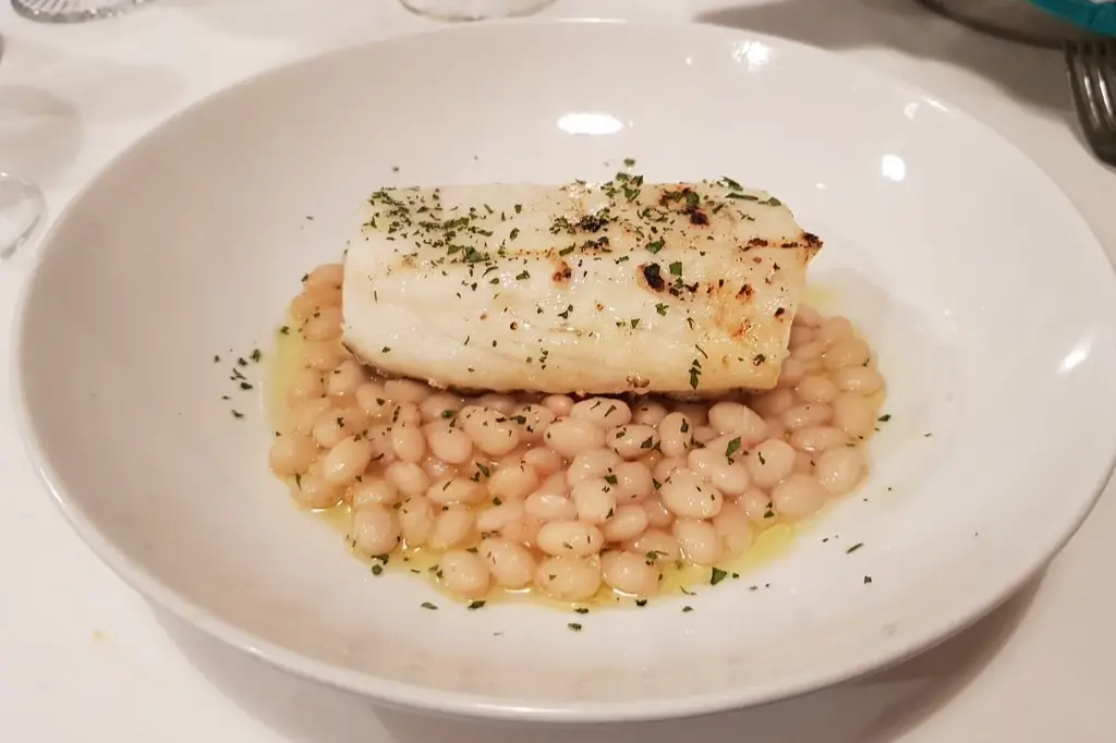 Grilled fish fillet with white beans and herbs on a white plate at Can Saia