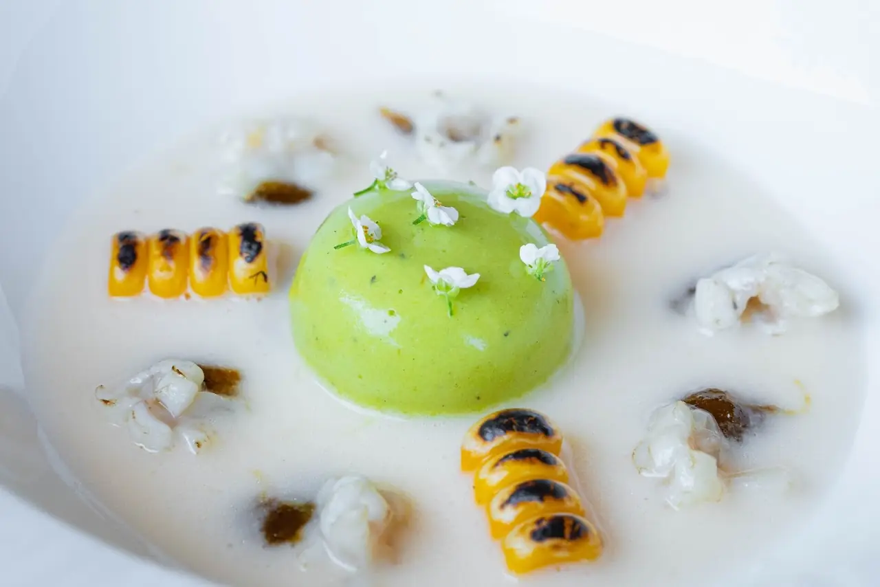 A bright green dome set in a pale broth, ringed with small orange rolls and white flowers