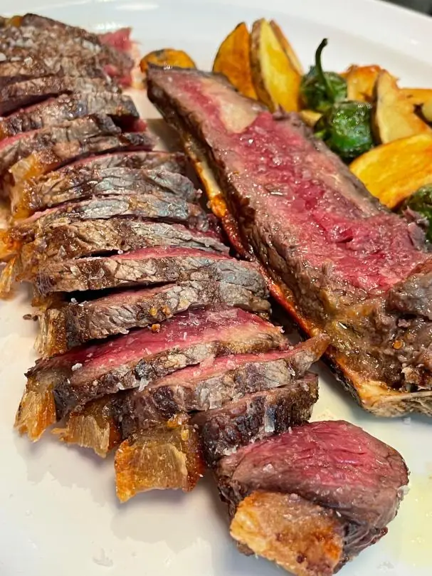 Close-up of sliced medium-rare steak with crispy edges, served with roasted potato wedges and blistered green peppers at Can Ugal
