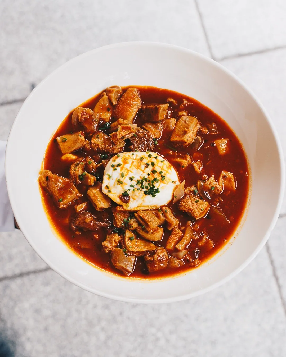 A white bowl of red stew with a spoonful of cream on top