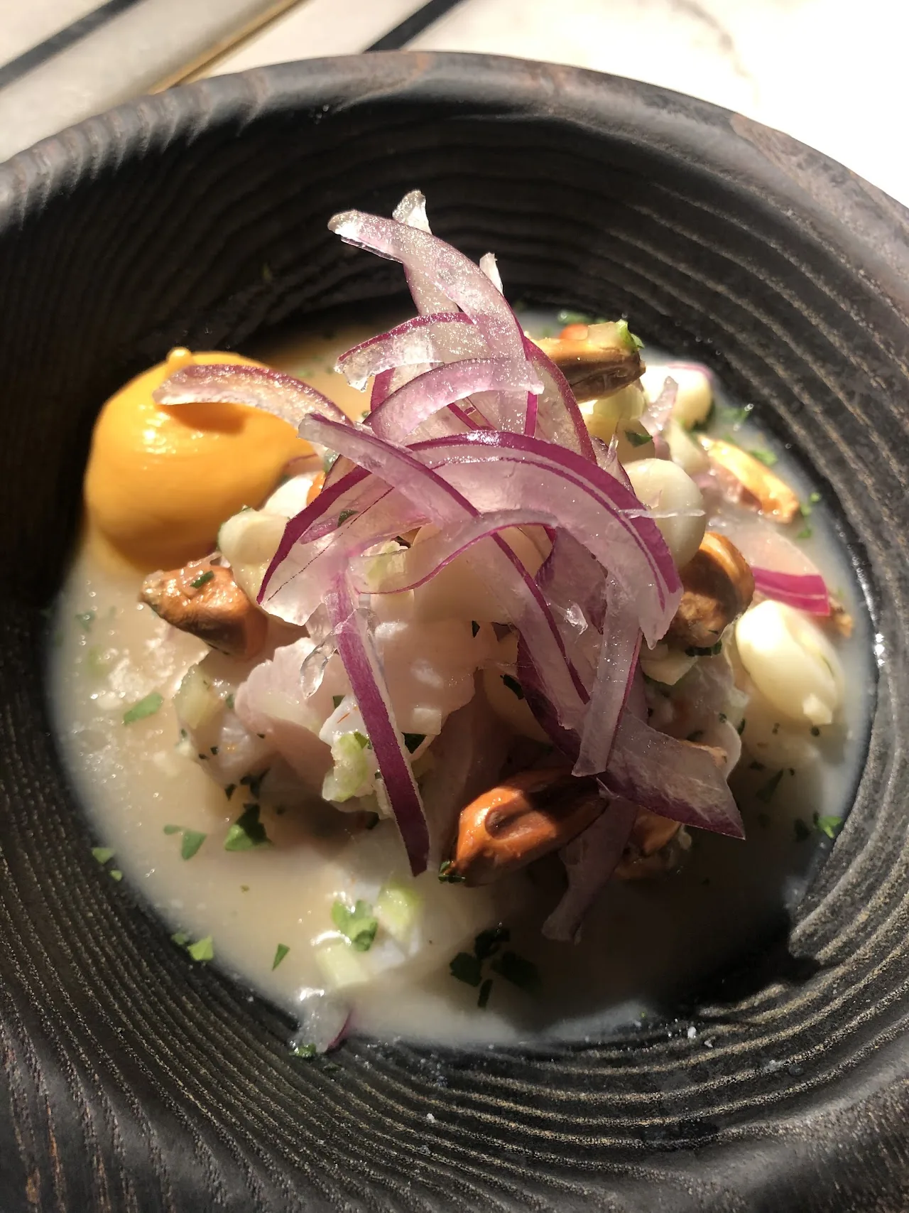 A ceviche dish with pickled red onion in a dark bowl