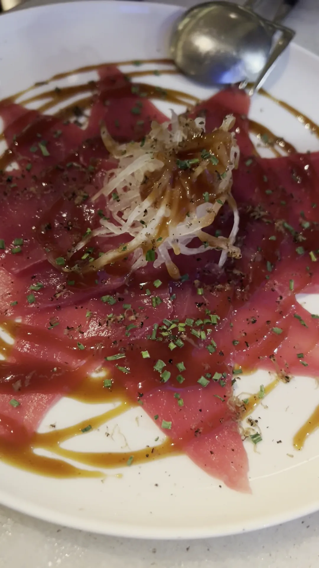Thinly sliced raw beef carpaccio with onion and herbs on a white plate