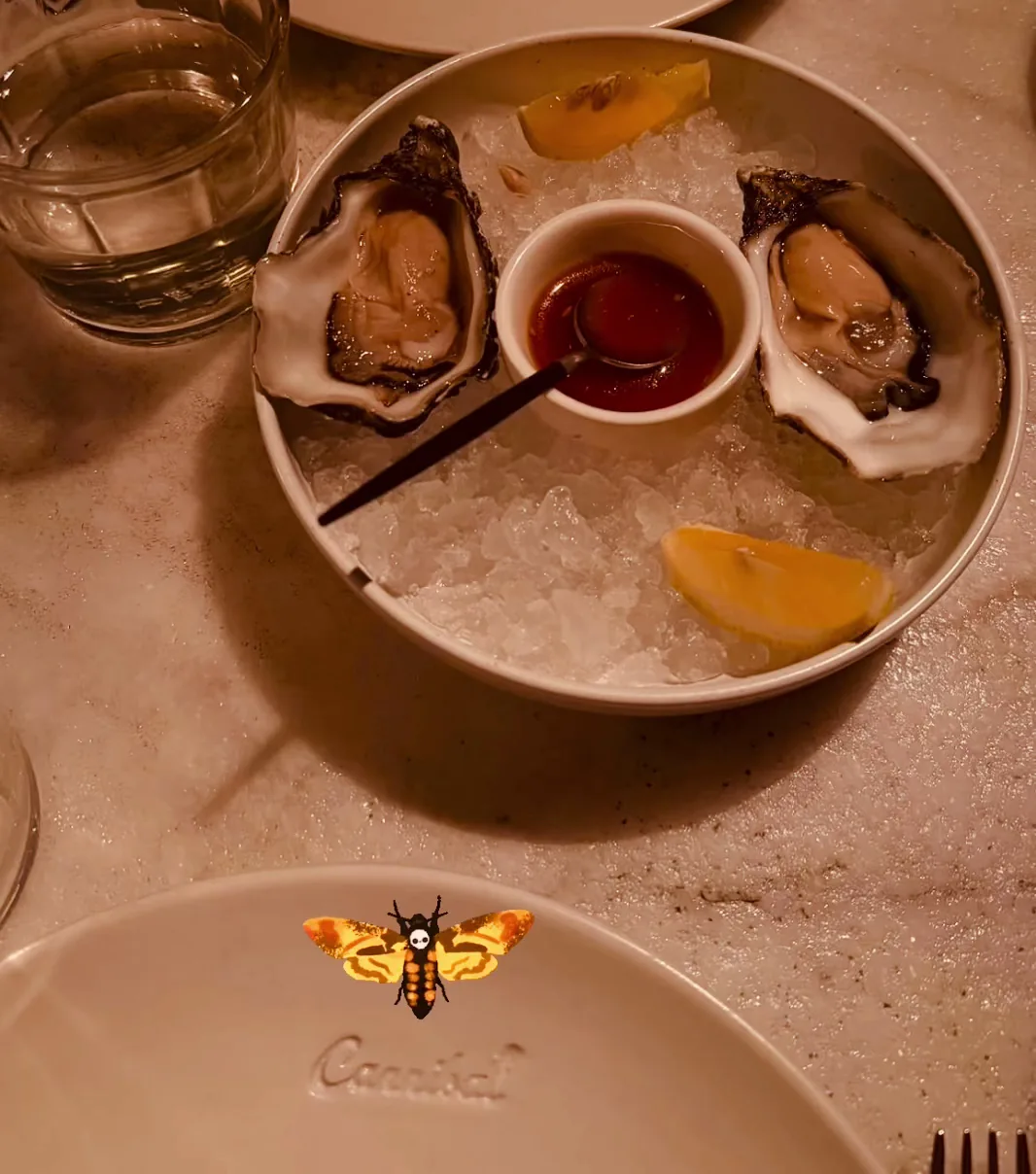A round platter of oysters on ice with lemon wedges and a hot sauce cup