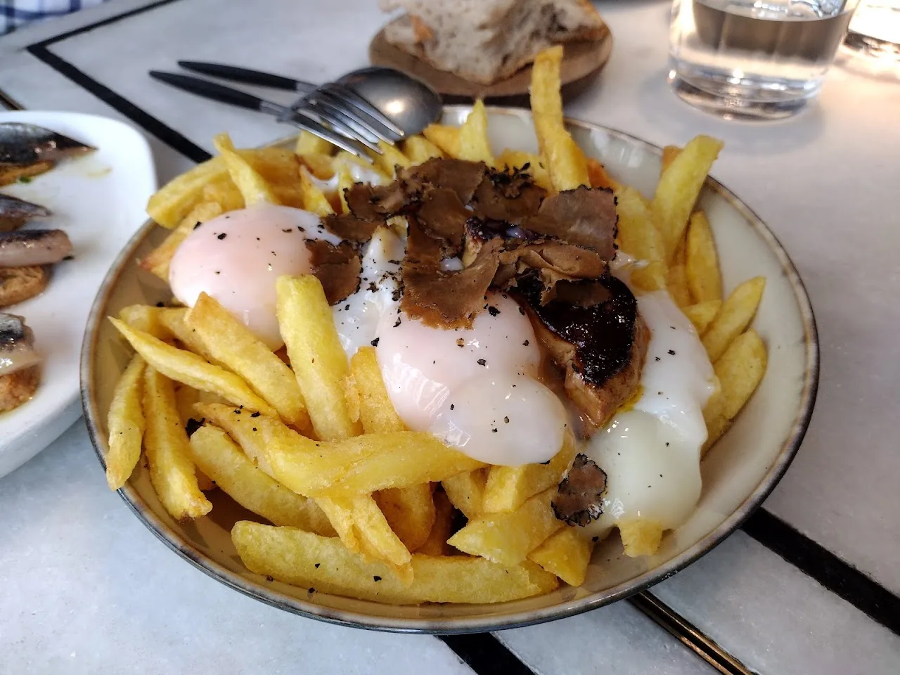 A plate of french fries topped with poached eggs and shaved truffle