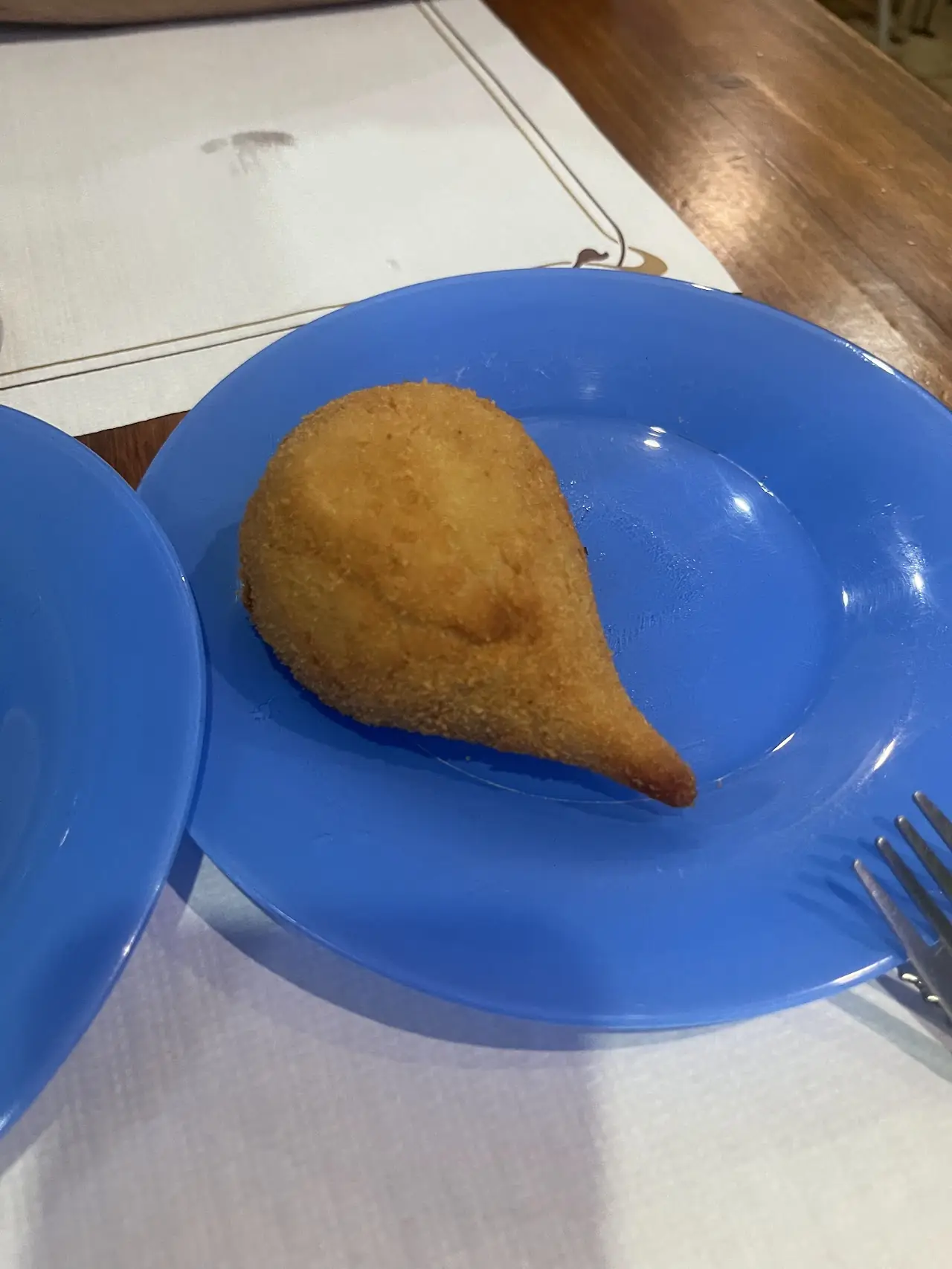 Coxinha, a teardrop-shaped Brazilian fried chicken croquette, on a blue plate, at Cantinho Brasileiro.