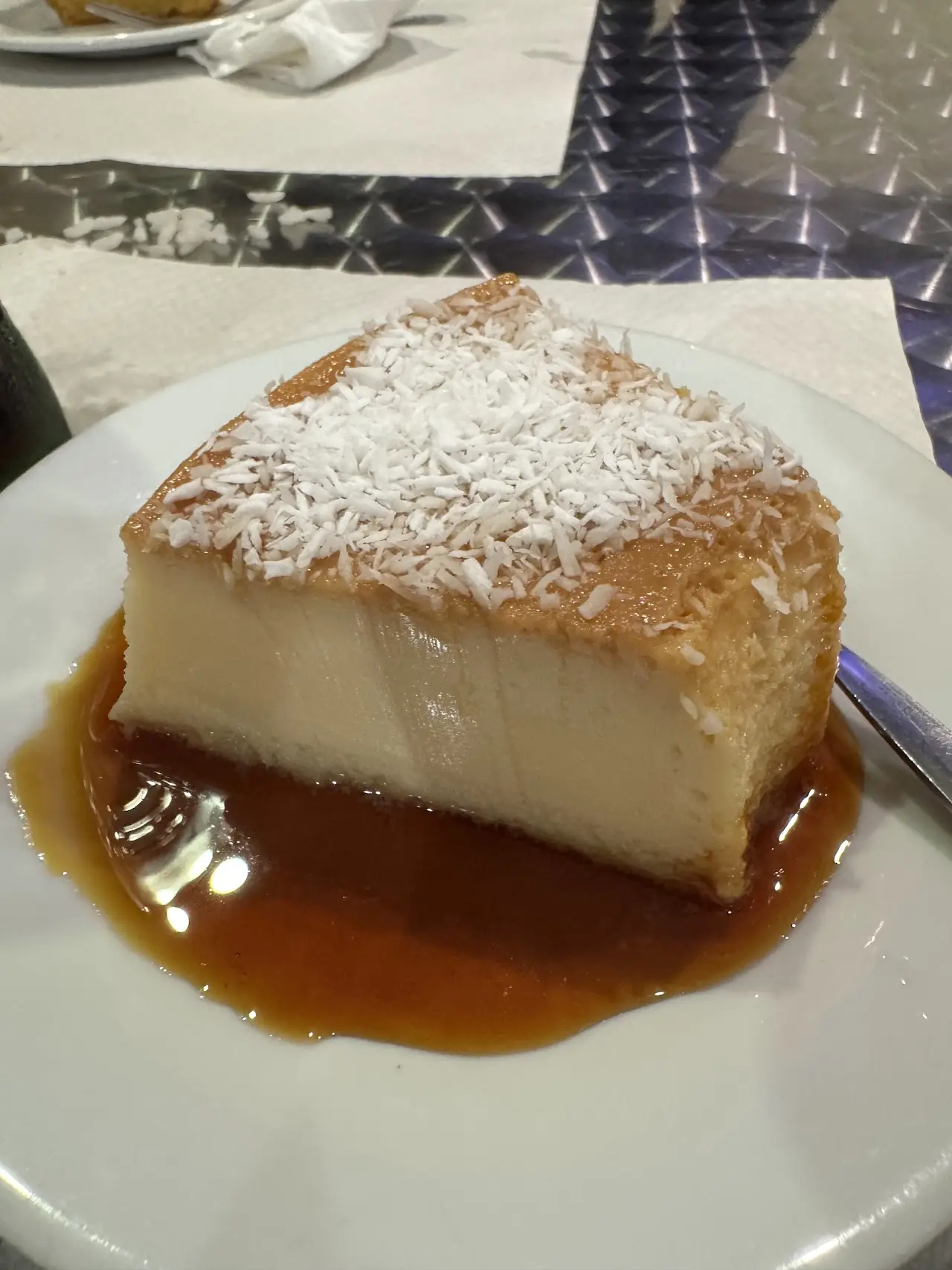 Pudim de leite (Brazilian caramel flan) topped with coconut on a plate, at Cantinho Brasileiro.