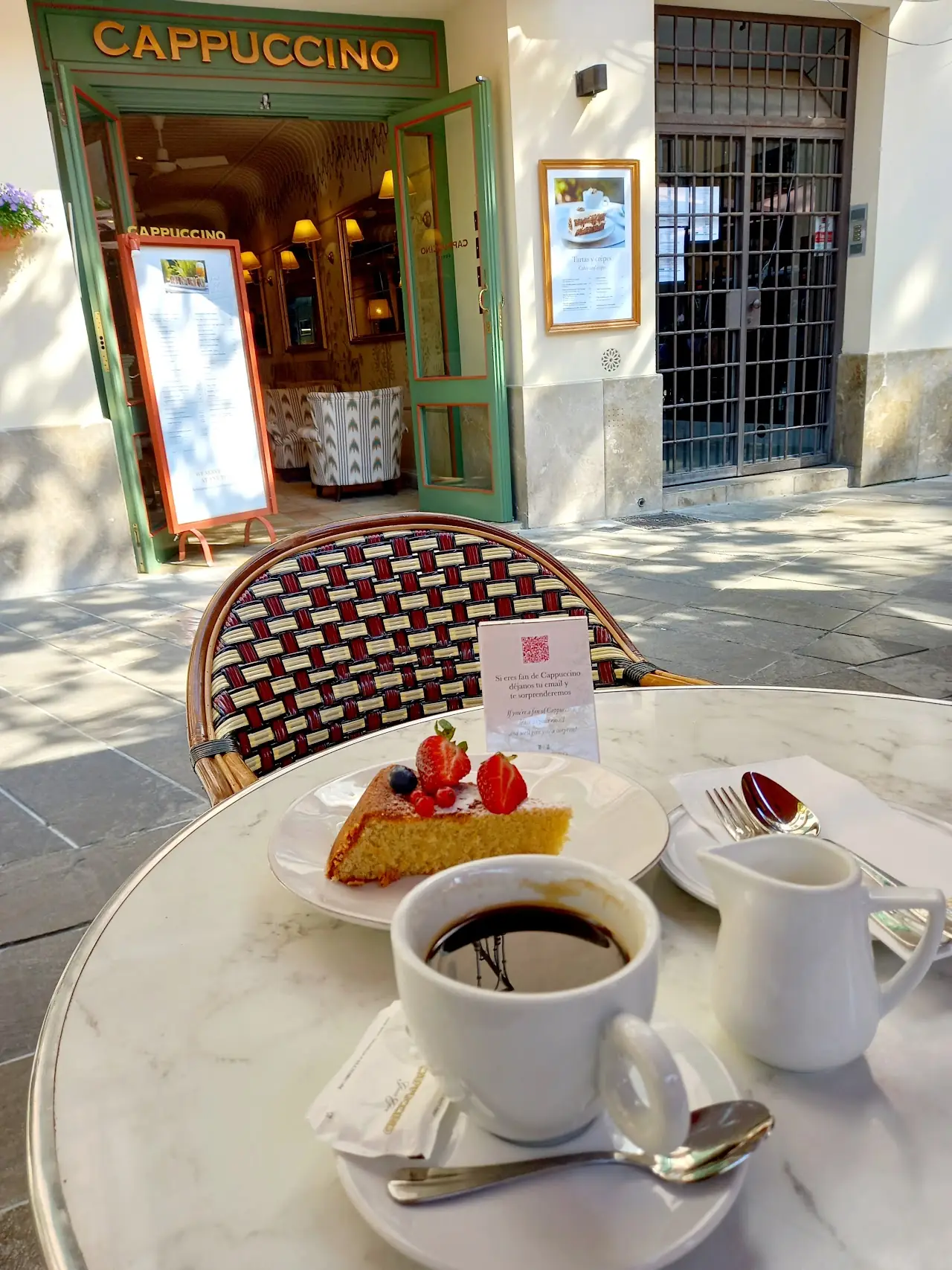 A slice of cake with strawberries and a coffee on a marble terrace table