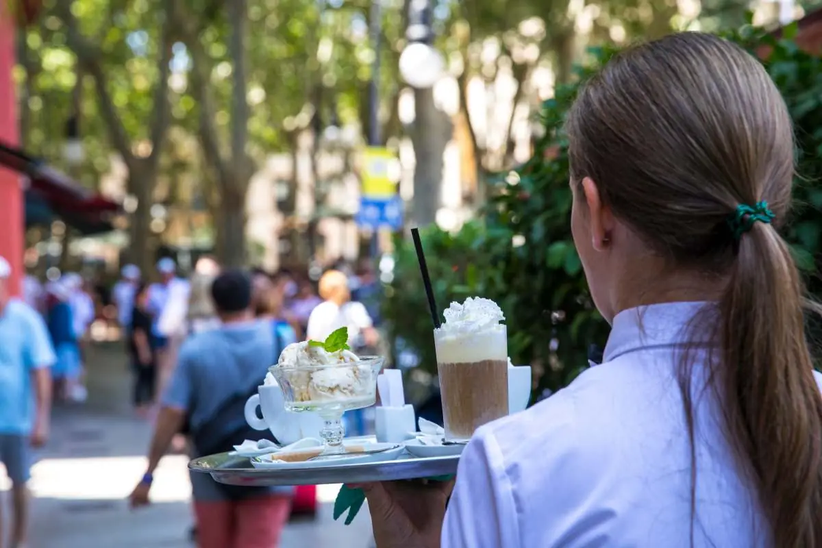 A waiter carrying iced coffees on a tray along the Born