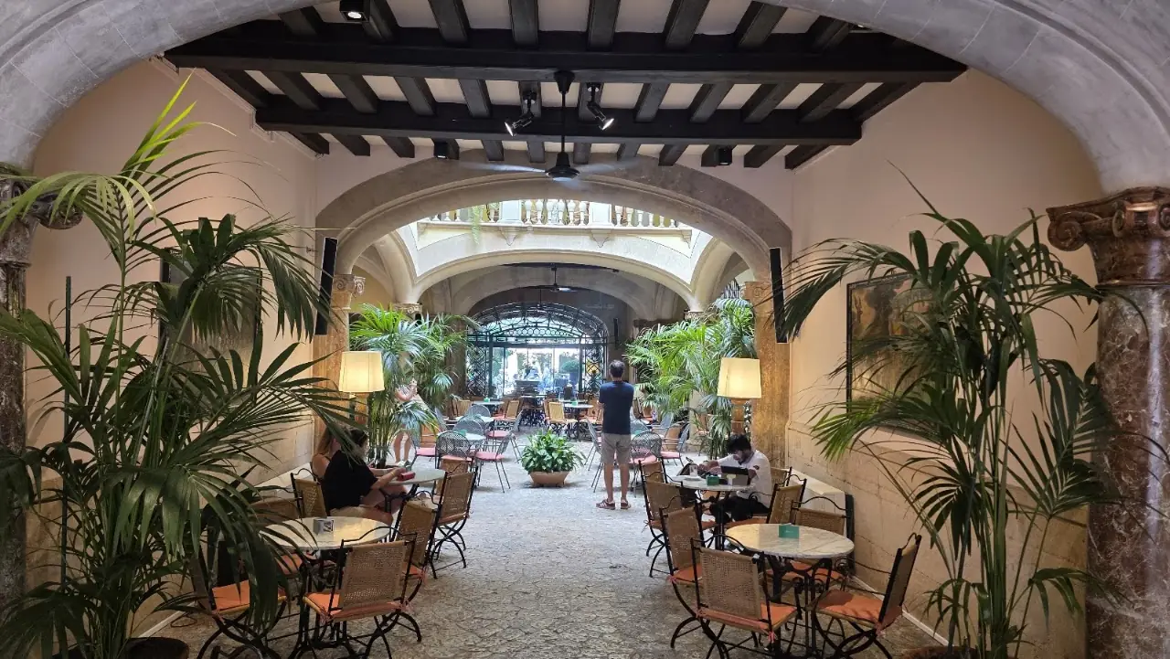 Tables set under the stone arcade with palms at the Palau March café