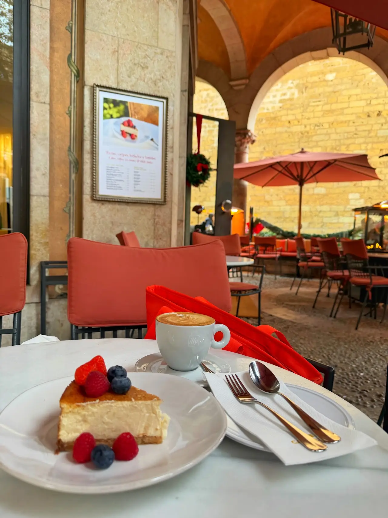 A slice of cheesecake with berries and a coffee on a terrace table