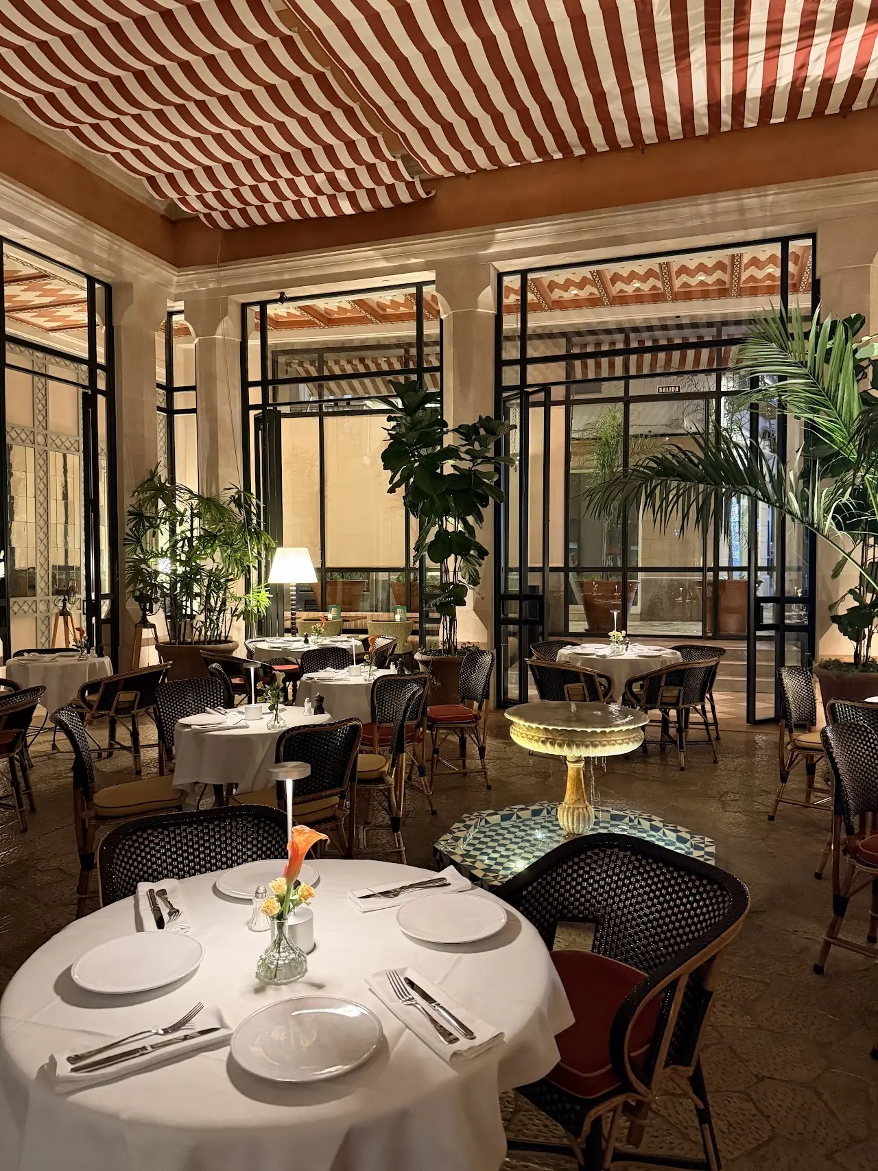 The glass-walled dining room with white-clothed tables and plants