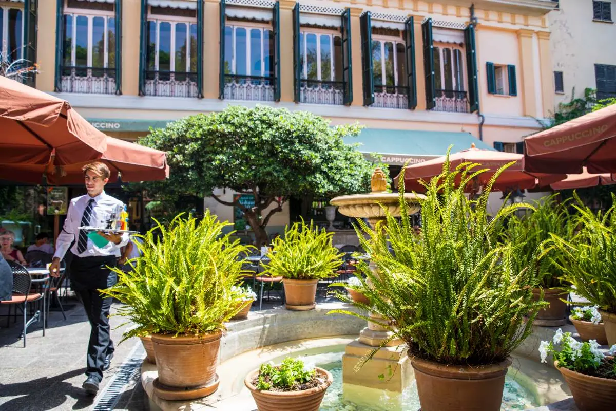 A waiter crossing the courtyard past the fountain with a tray