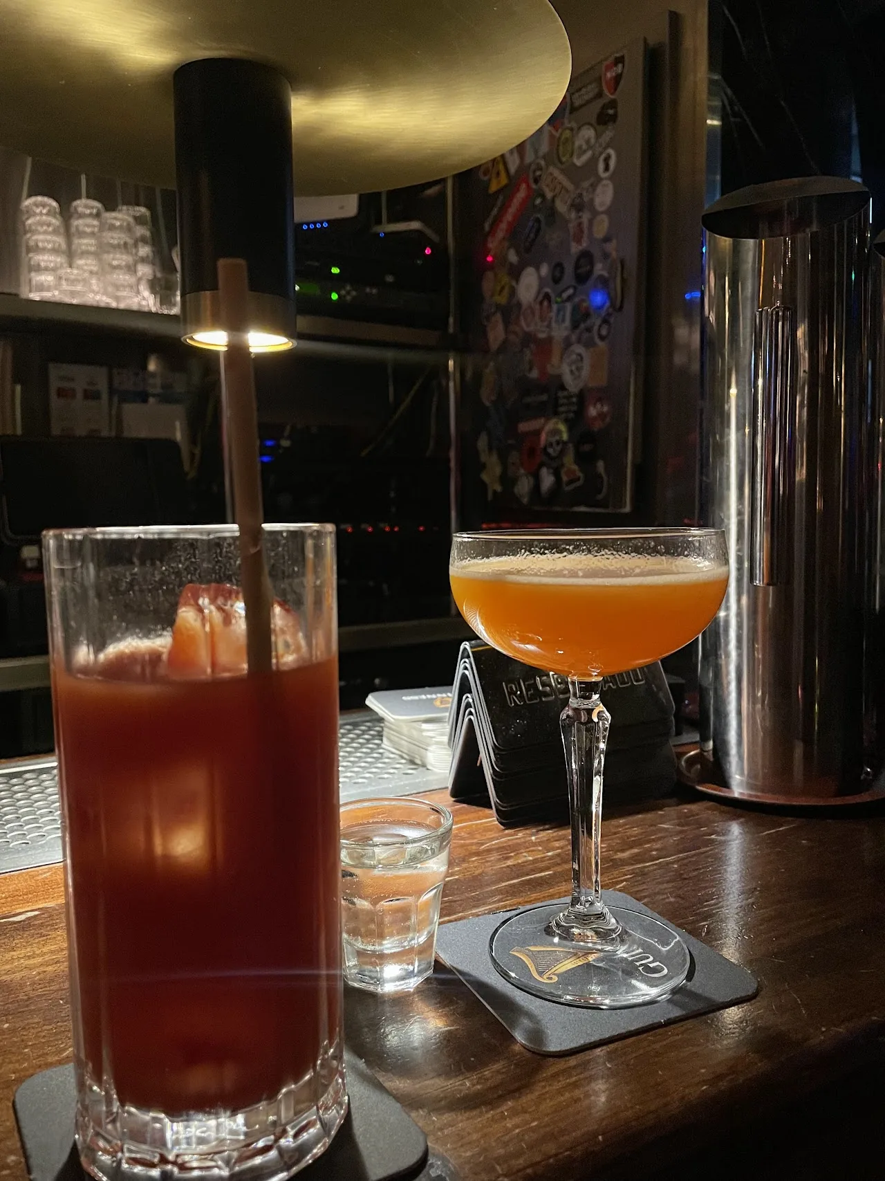 Two cocktails on a bar, one in a coupe glass and one in a highball glass with ice