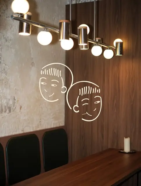 Dining-room corner with two line-drawn faces on a walnut wall, banquette seating and a globe pendant light
