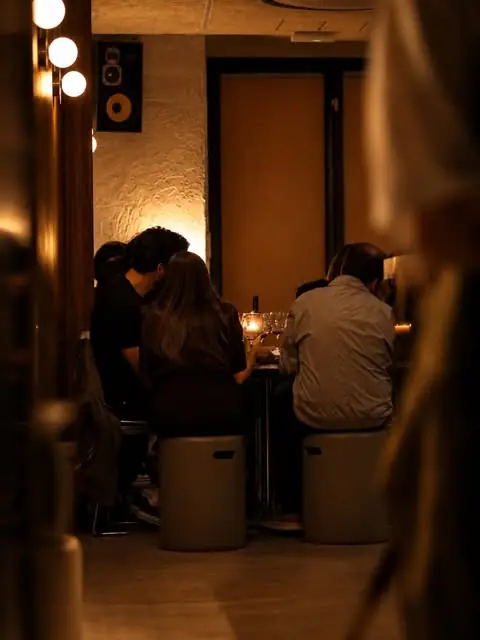 Warm candlelit bar interior with diners seated on stools around a small table