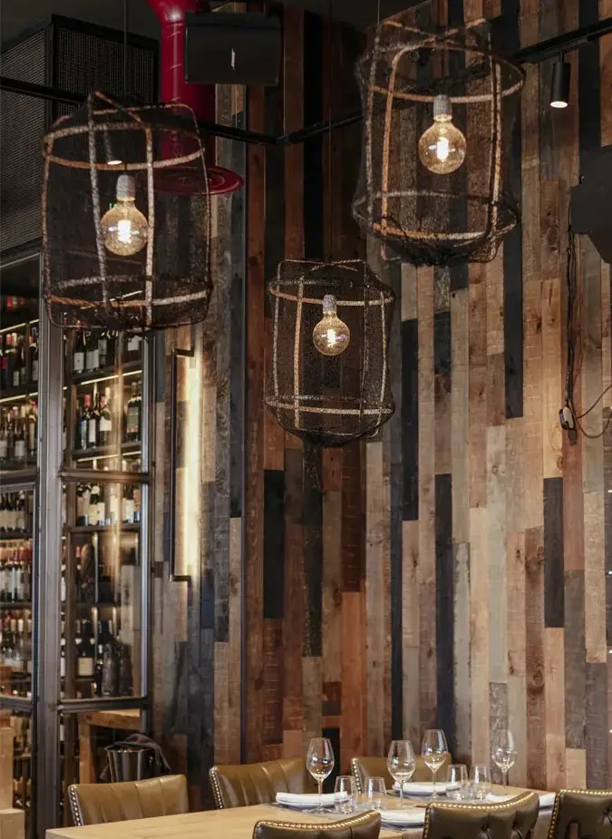 Dining room with woven rope pendant lights over a set table, wood-plank wall and glass-fronted wine cabinet
