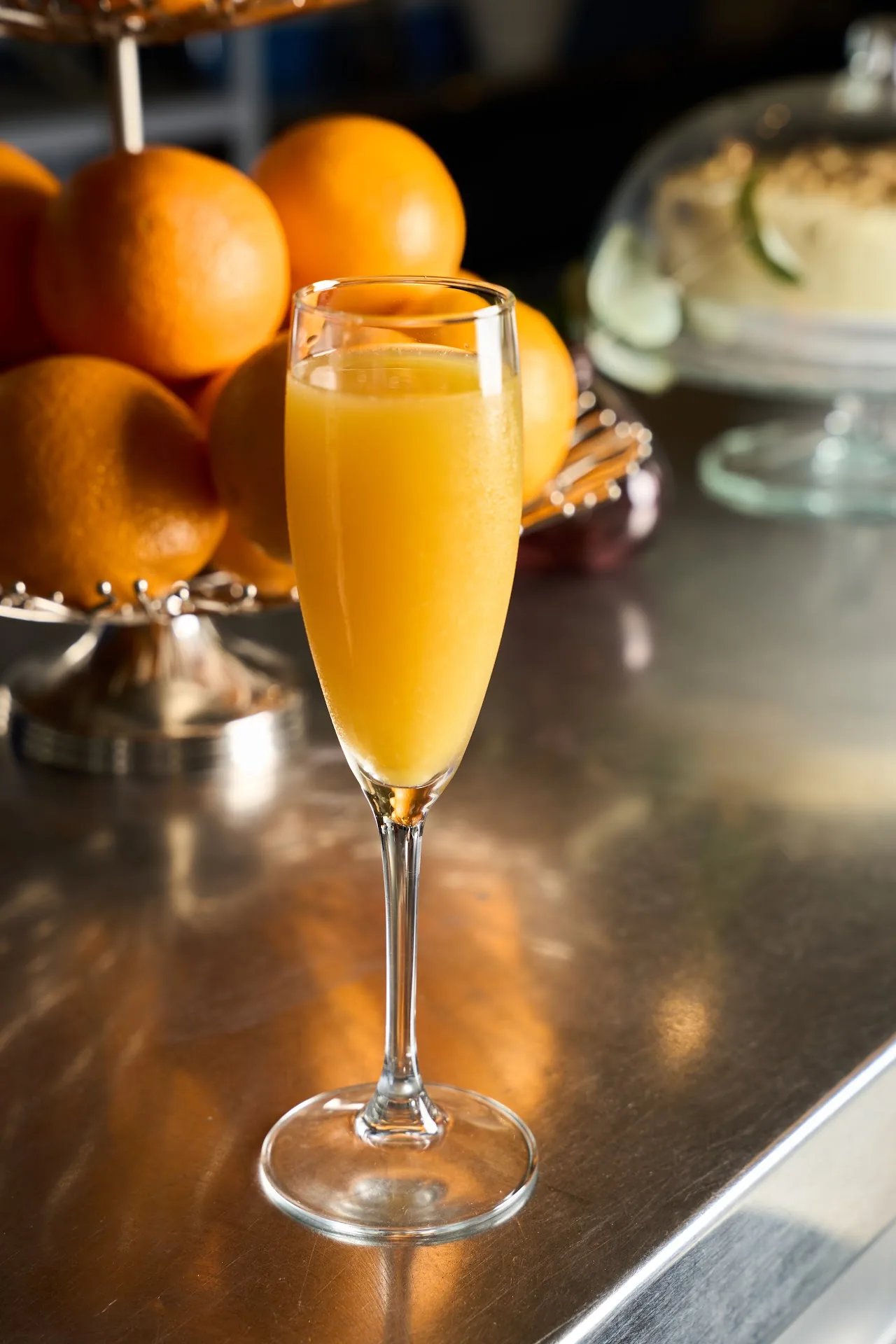 A mimosa in a champagne flute on a bar counter with oranges in the background