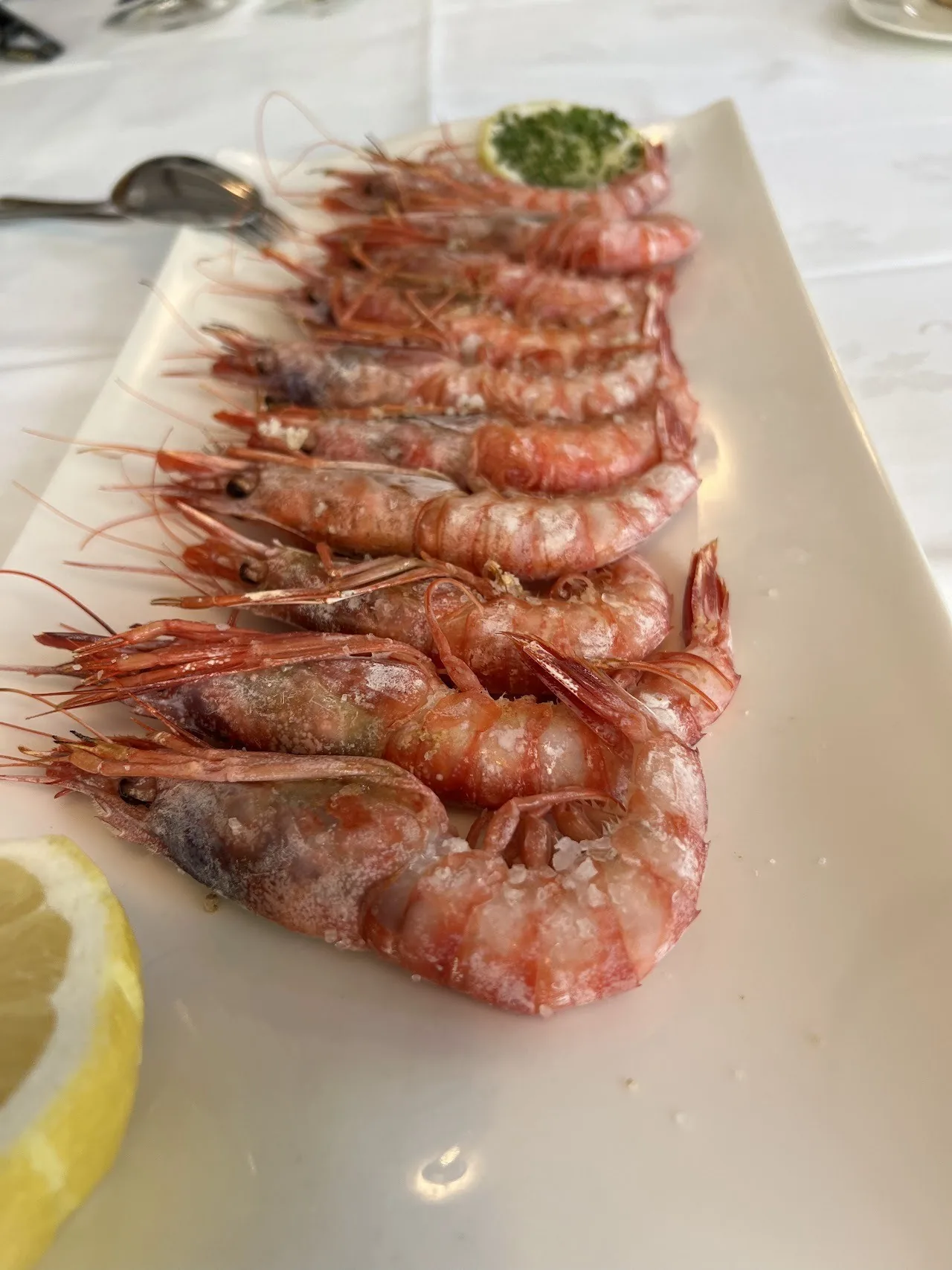 A row of cooked prawns on a long white plate with a lemon wedge