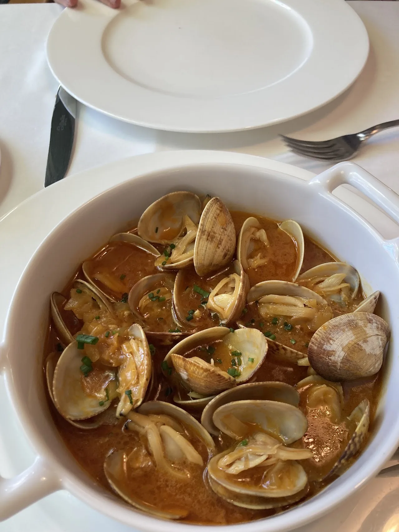 A white pot of clams in a light broth