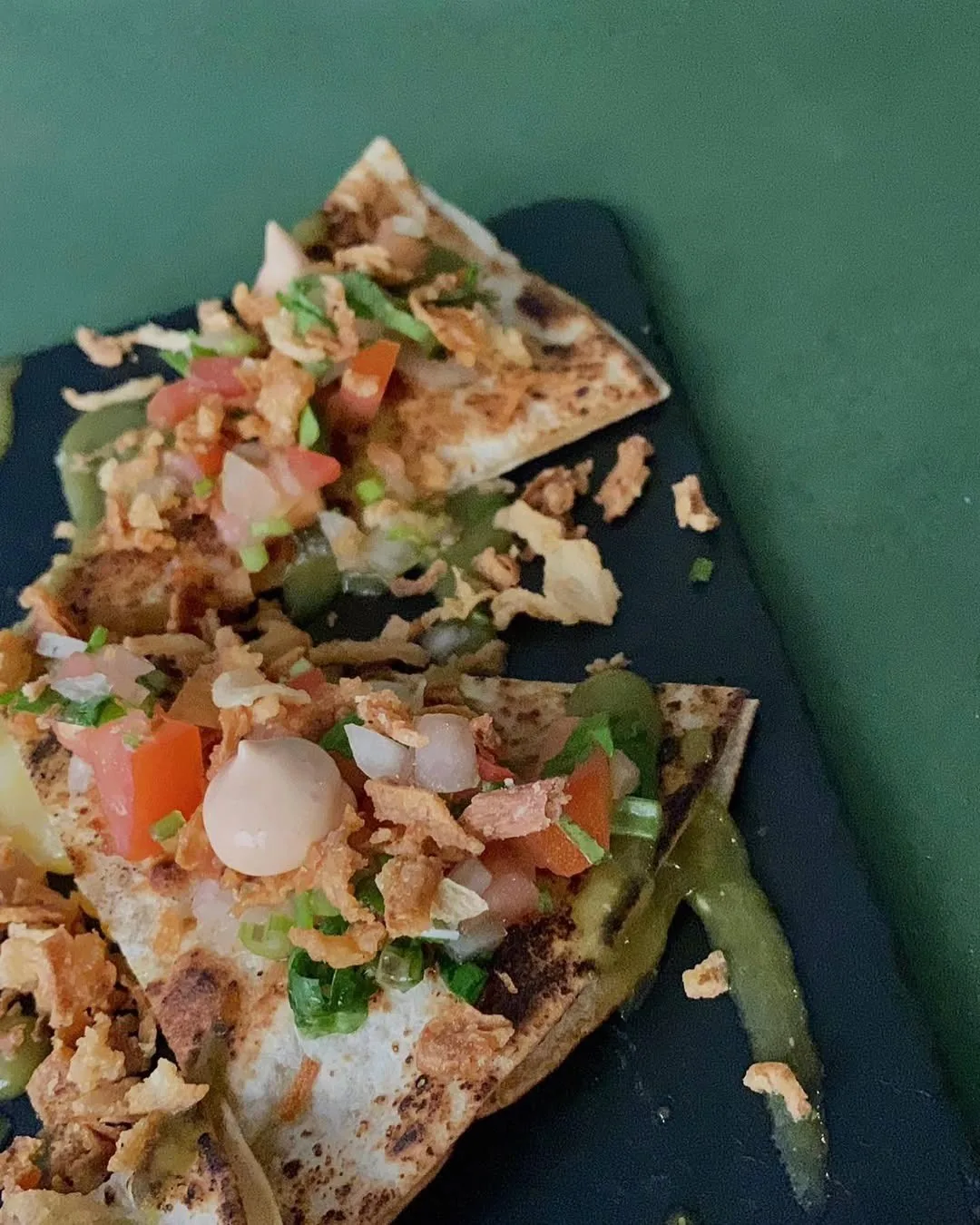 A crisp flatbread topped with meat, diced tomato and onion on a dark board