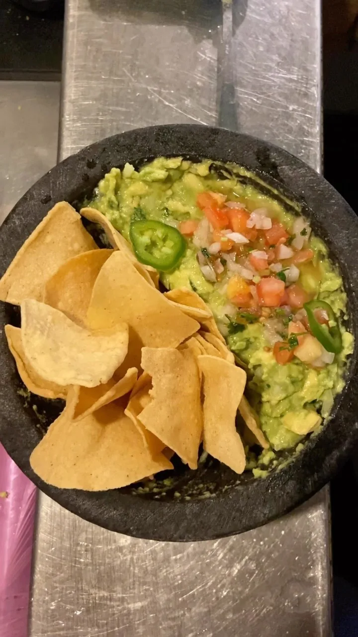 Guacamole topped with diced tomato, onion, and jalapeño slices, served in a stone molcajete with tortilla chips