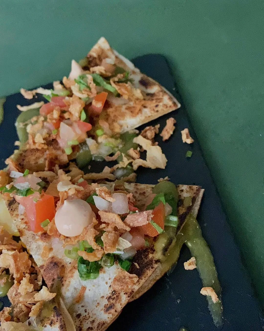 Toasted quesadilla wedges topped with pico de gallo, crema, and crispy onions on a dark board