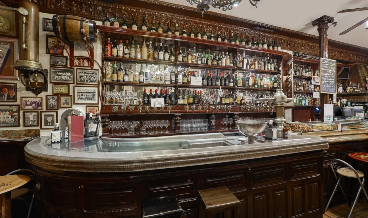 A curved zinc-topped wooden bar counter with shelves of bottles behind it