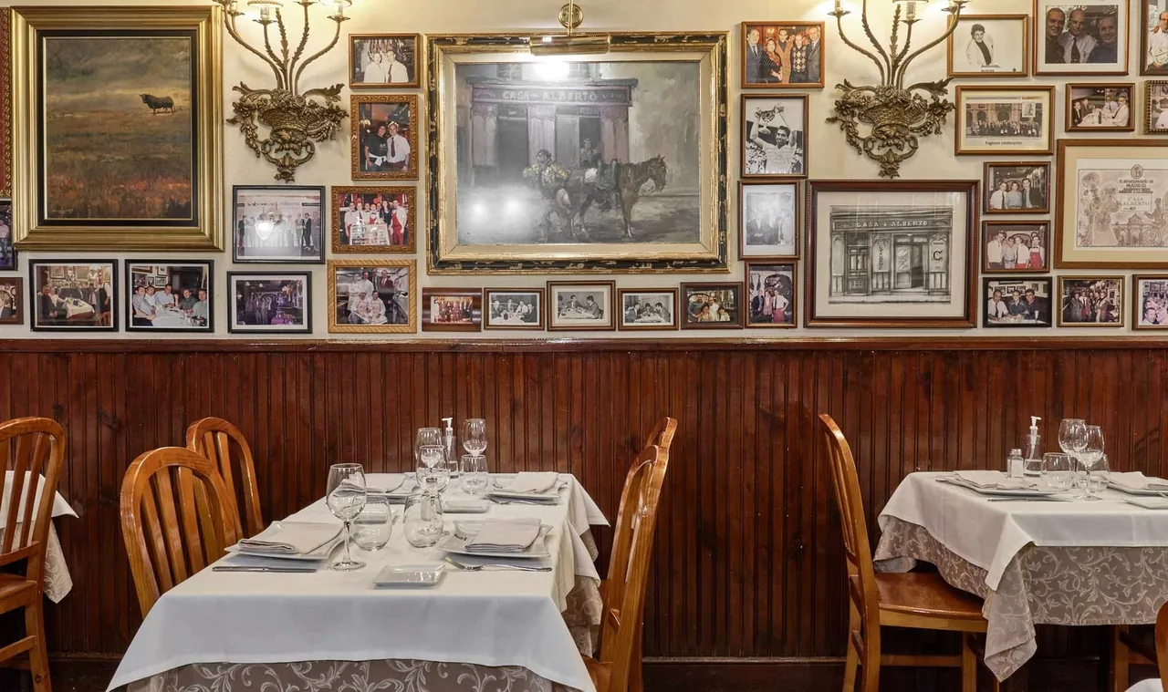 A dining room with wood panelling, framed pictures on the wall and tables with white tablecloths