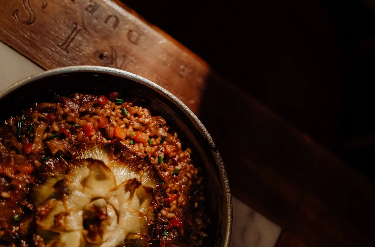 Rice with mushrooms, diced peppers, and a whole roasted artichoke in a metal pan at Casa Alfonso