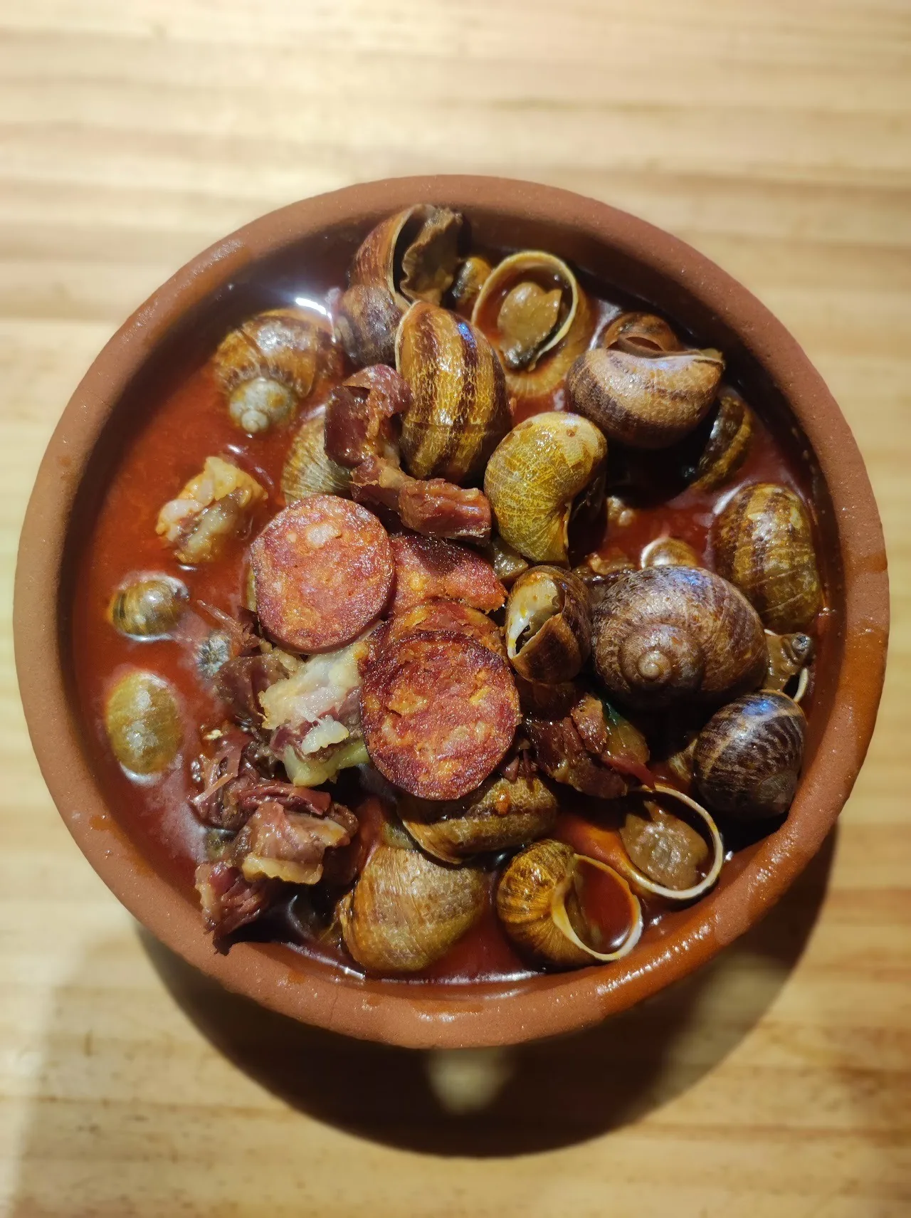 A round earthenware dish of snails with chorizo in sauce