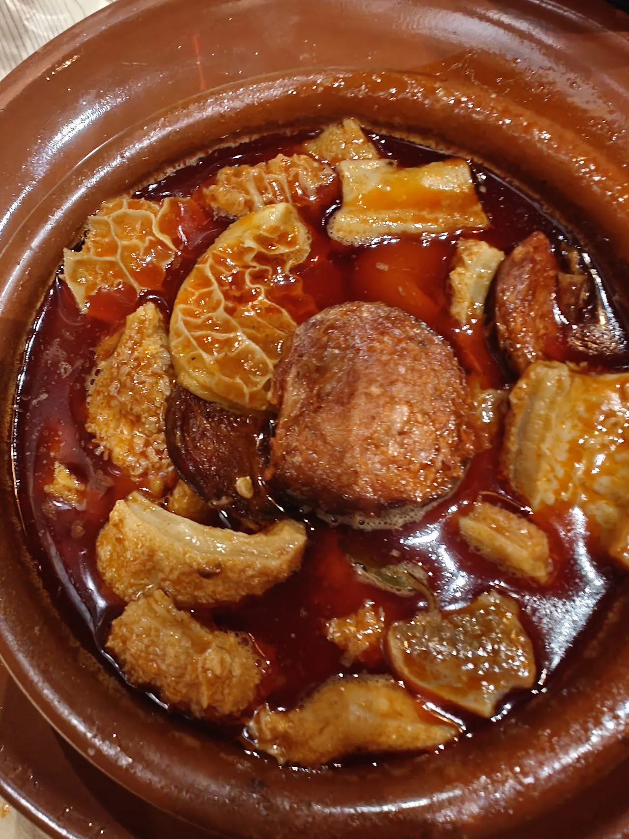 A terracotta dish of roasted pork ribs and belly with a honey glaze