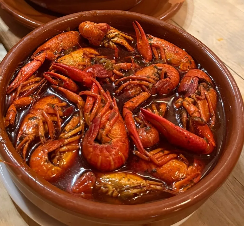 A terracotta bowl of whole crayfish in a spicy red sauce