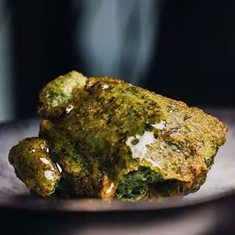 Green herb-crusted croquette or fritter with a glossy sauce on a dark plate, Casa Amàlia 1950 Port Vell