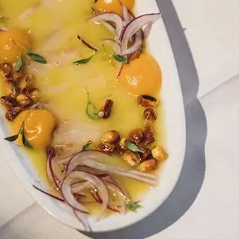 Sliced fish carpaccio plated with red onion rings, citrus sauce, and toasted nuts, Casa Amàlia 1950 Port Vell