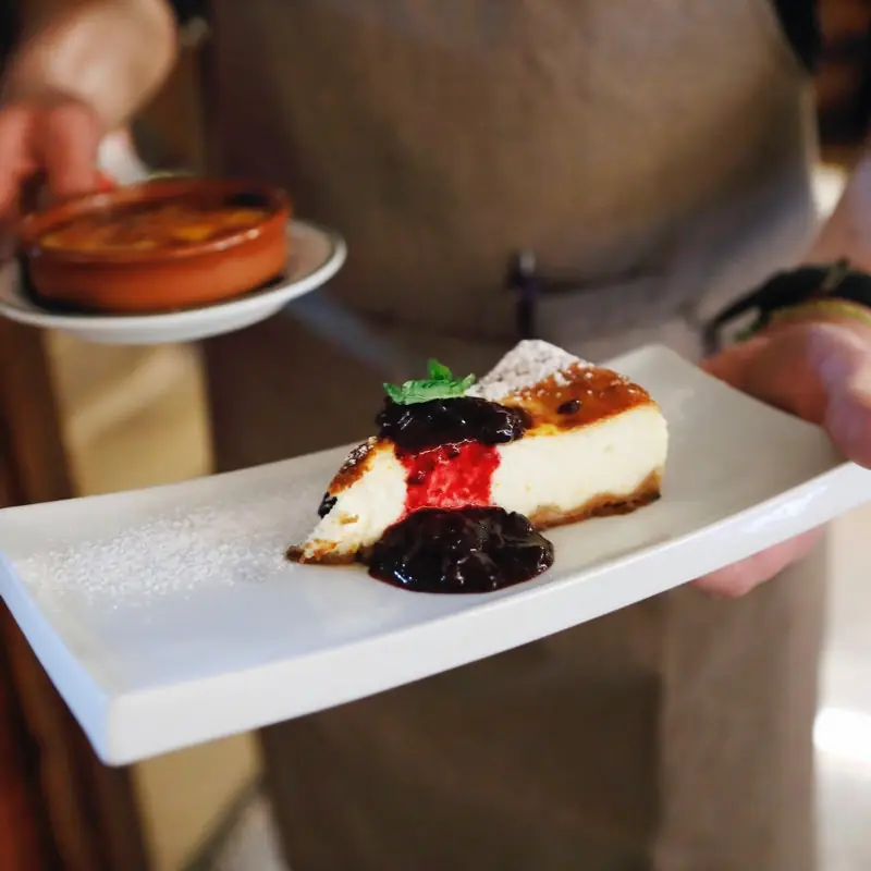 Slice of baked cheesecake topped with mint and a berry compote, served alongside a small clay dish of crema catalana, at Casa Ángela