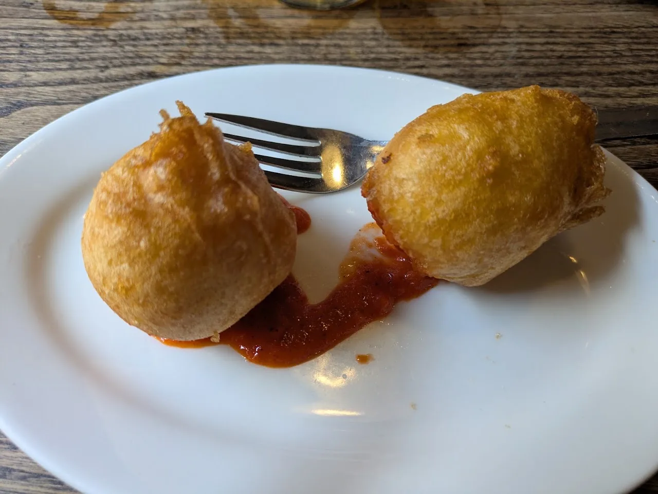 Two fried croquettes on a plate with a swirl of red sauce