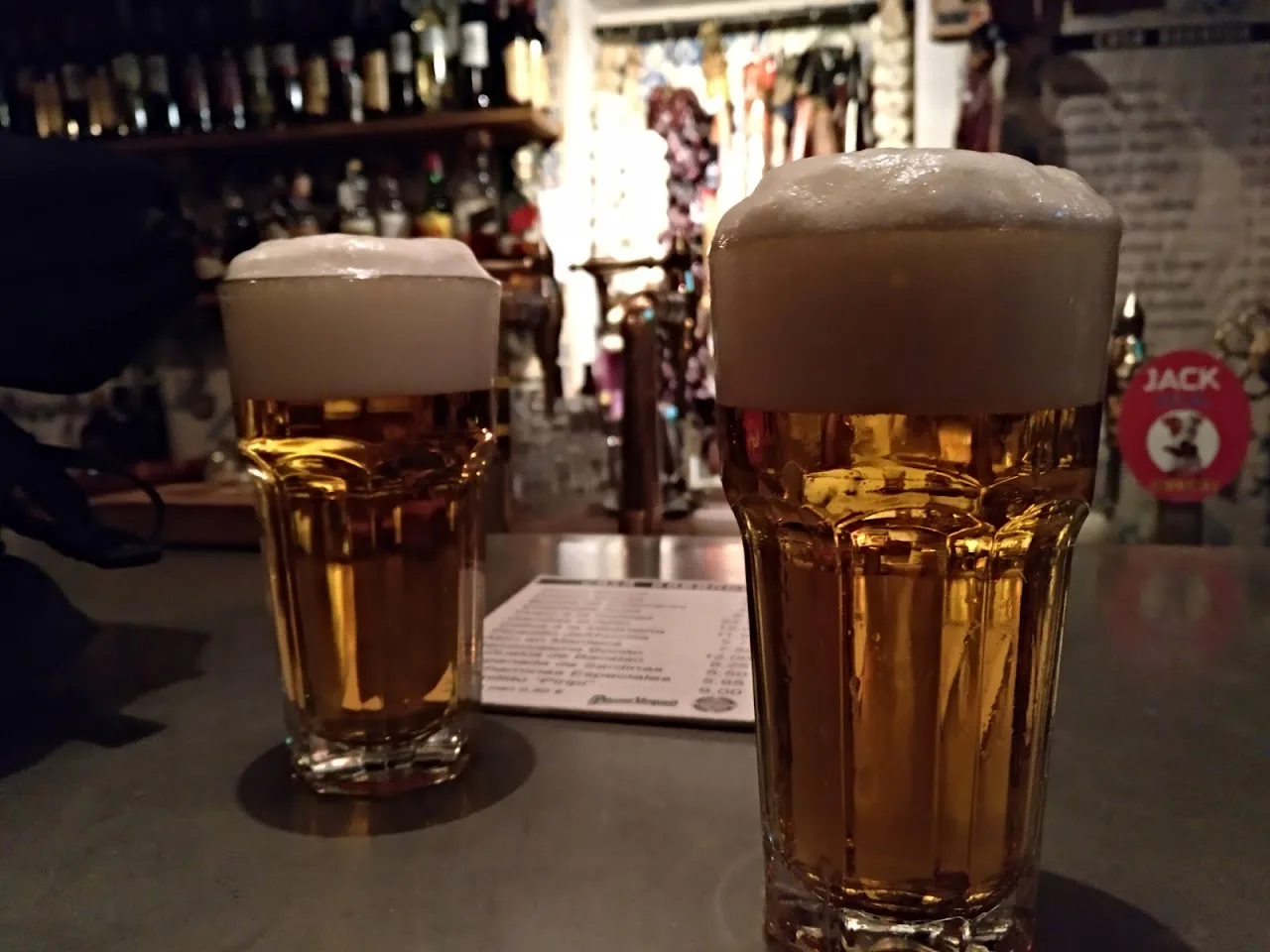 Two glasses of draft beer with foam heads on a bar counter