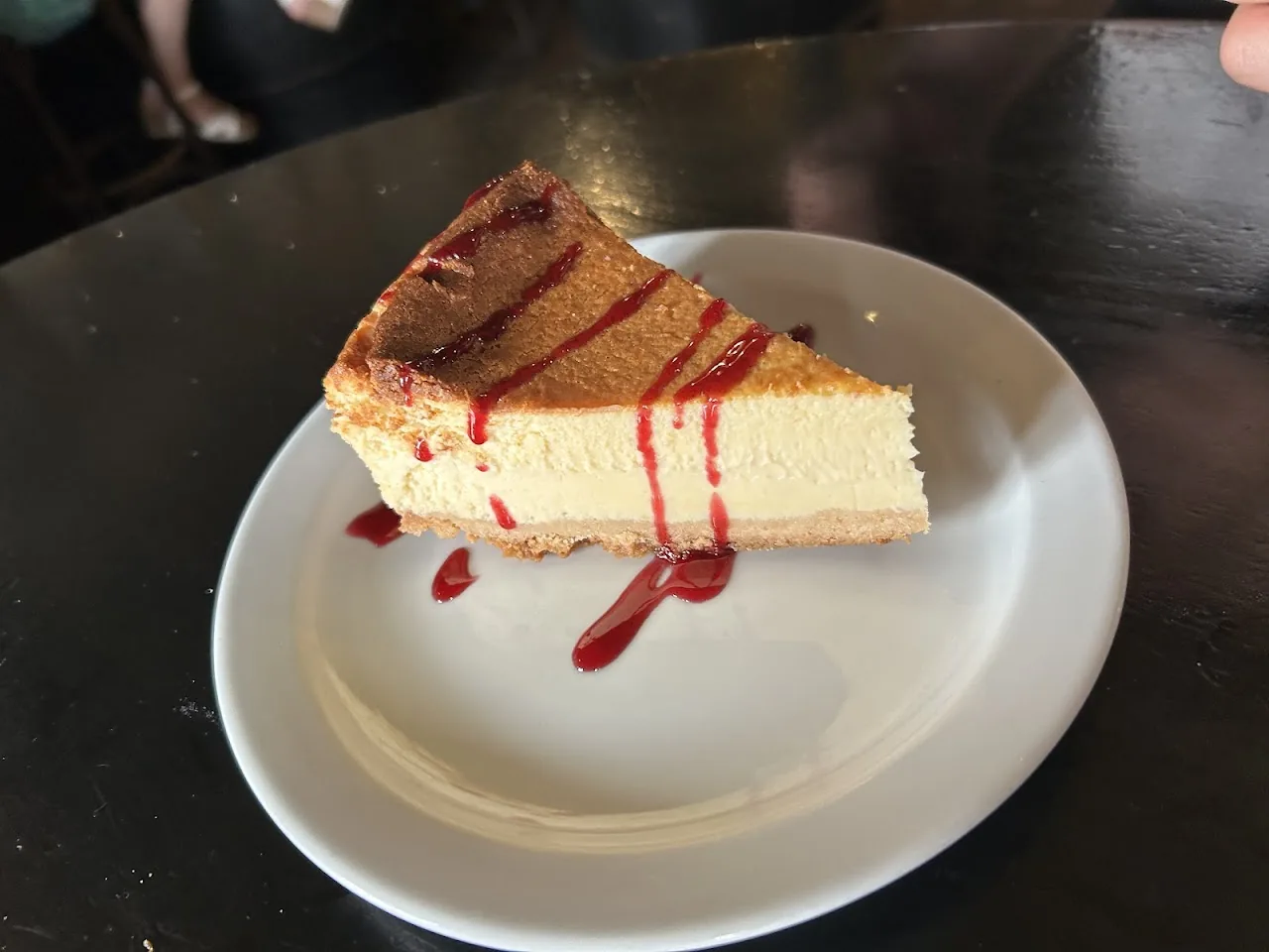 A slice of cheesecake drizzled with red berry sauce
