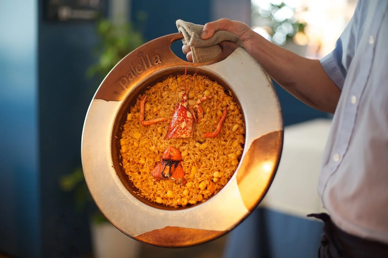 A paella pan of saffron rice with shellfish being presented tableside