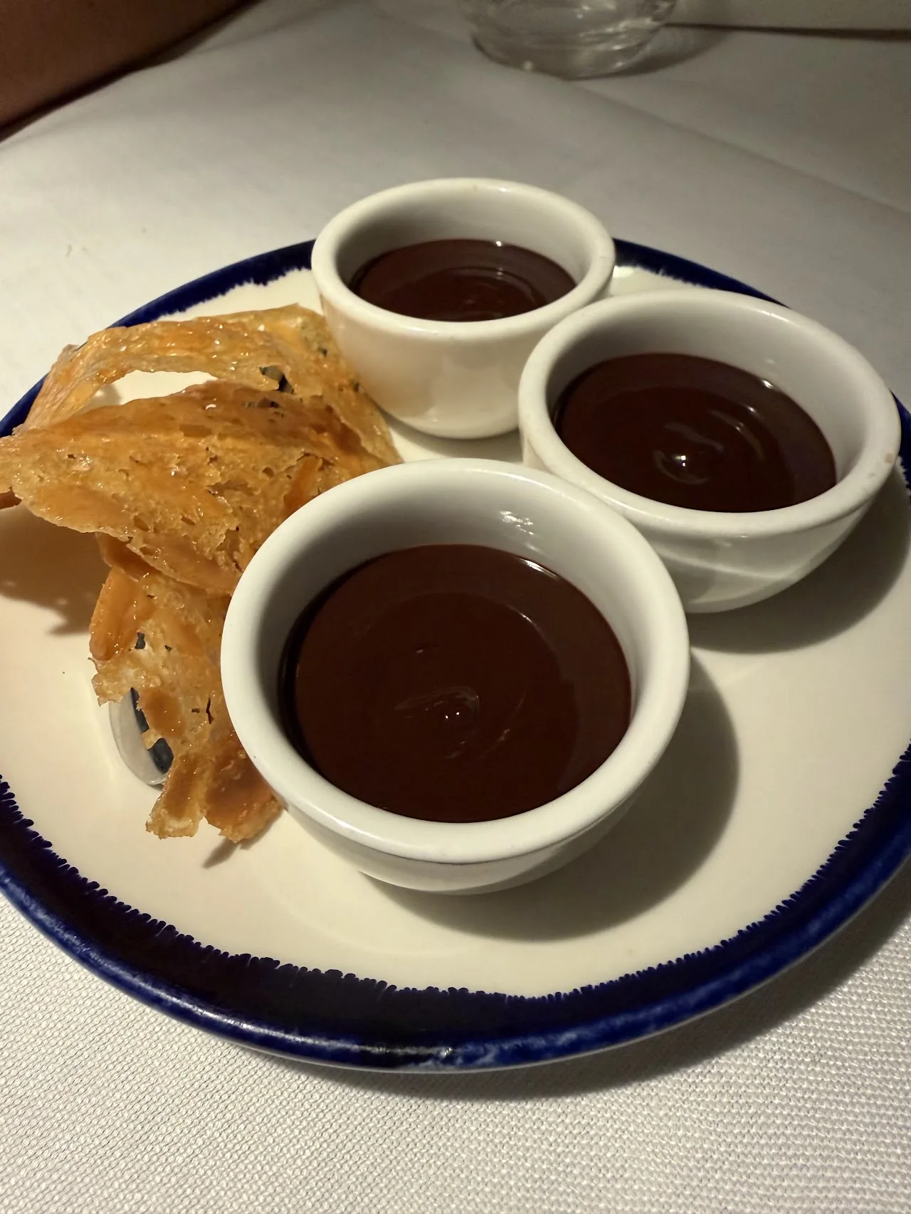 Three small cups of chocolate sauce beside pieces of fried bread for dipping