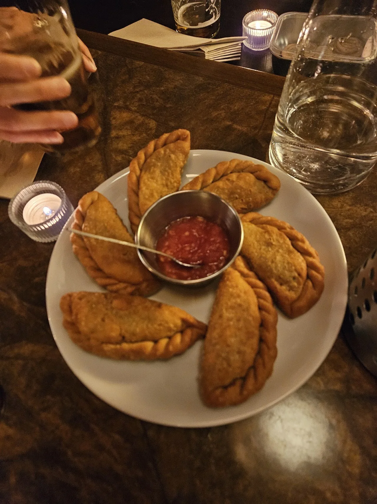 A plate of golden empanadas with a small dish of sauce