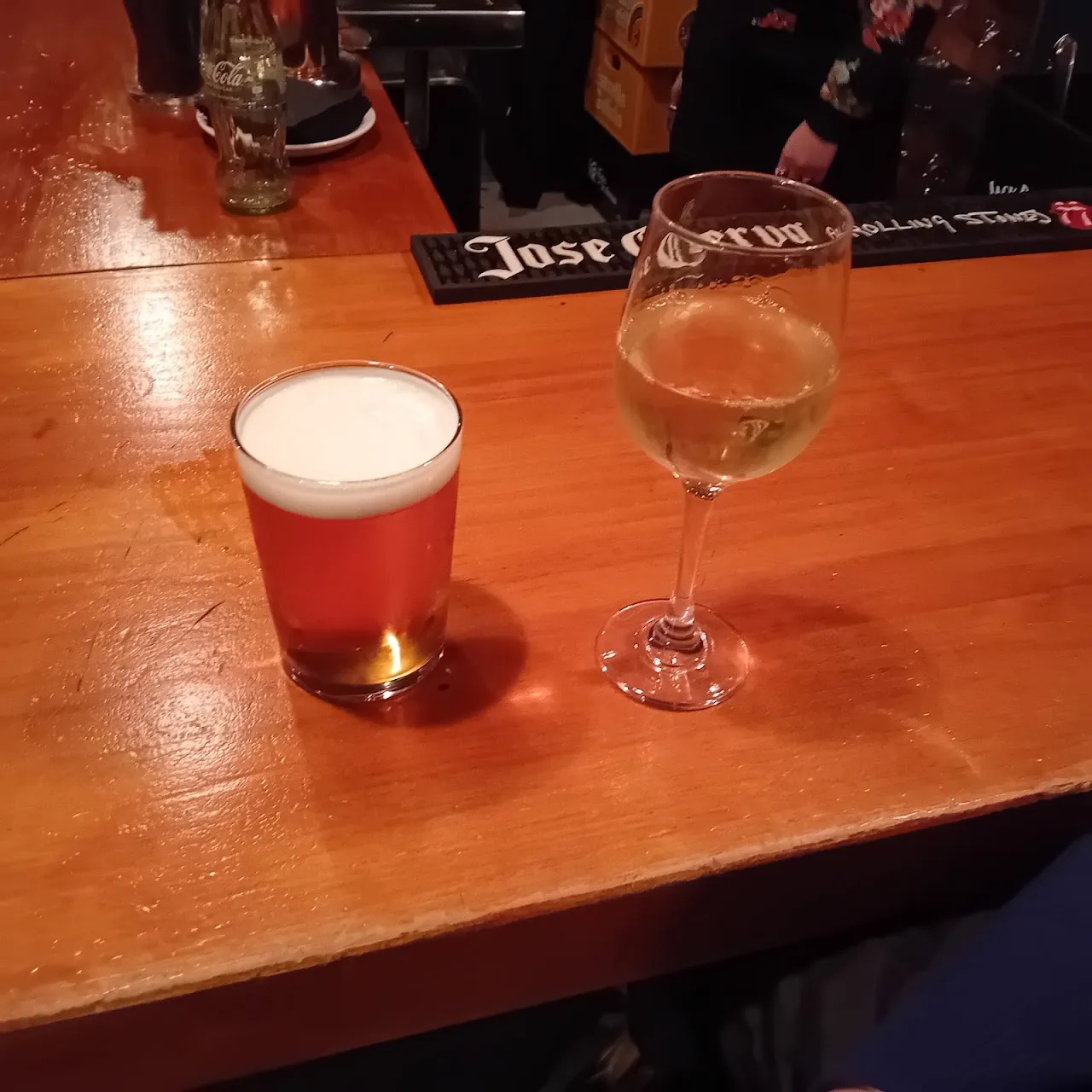 A glass of beer and a glass of white wine on a wooden bar counter