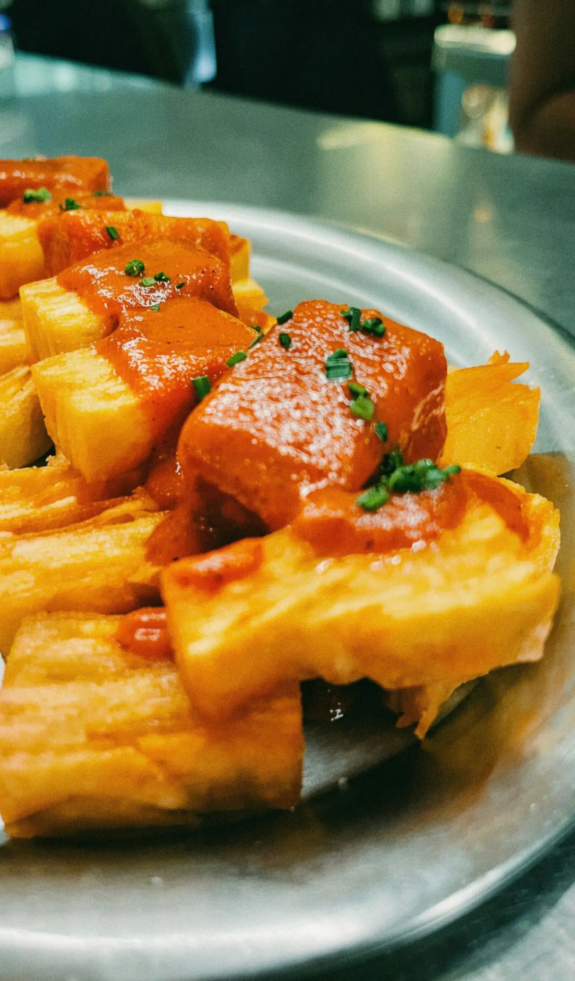 Bravas made from layered potato millefeuille, with spicy brava sauce and herbs, on a metal plate