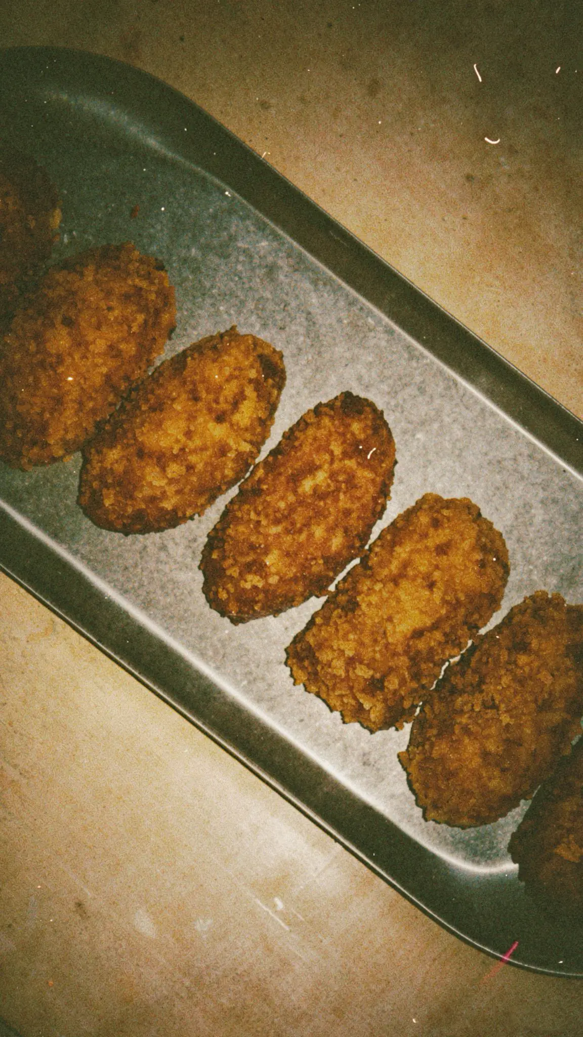 A row of breaded croquetas on a metal tray