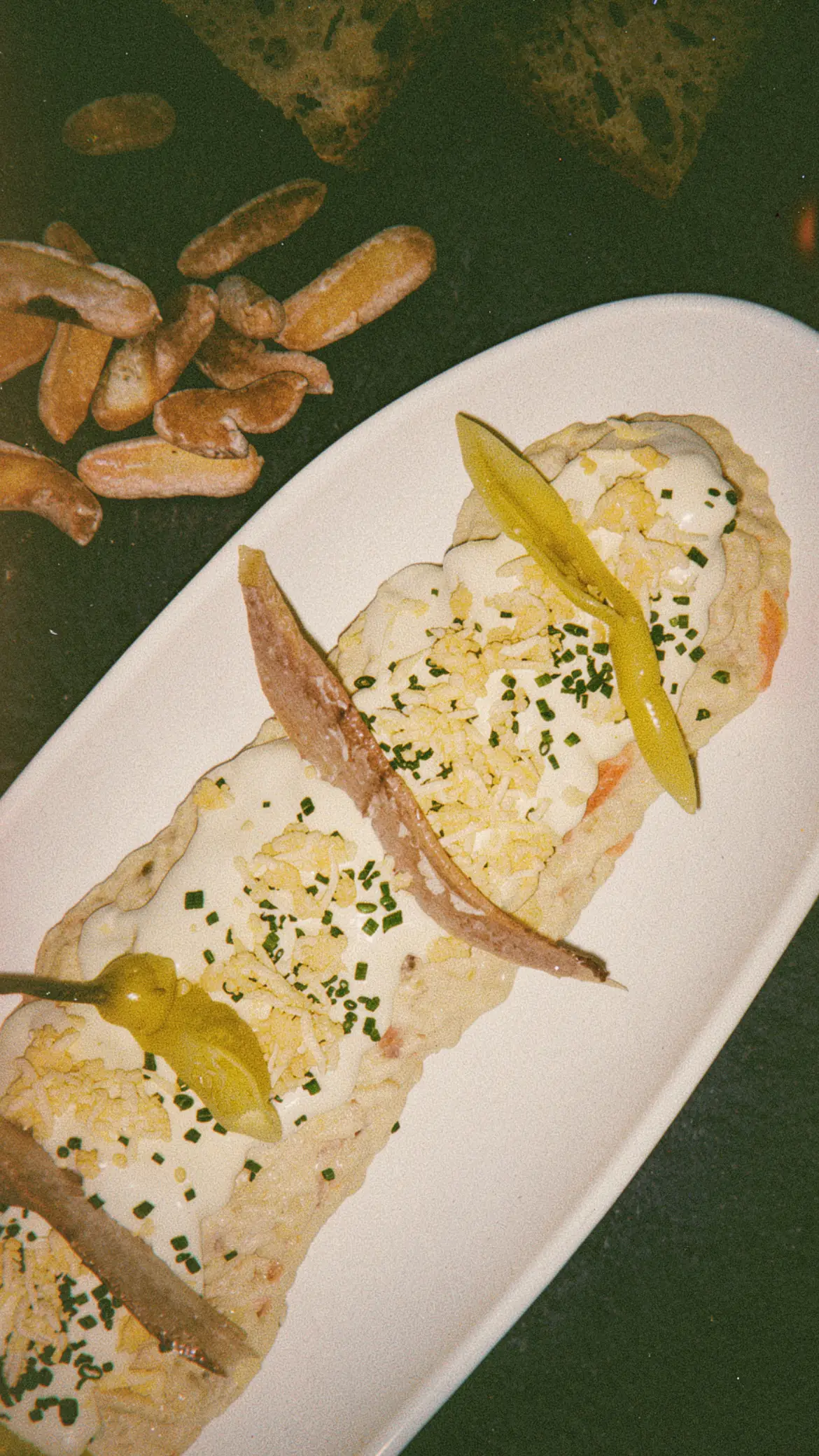 A creamy salad topped with anchovy fillets and pickled guindilla peppers on an oval plate