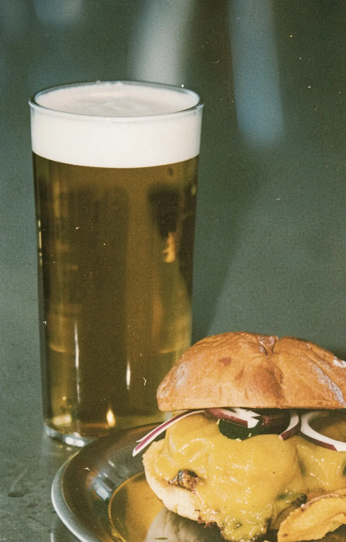 A cheeseburger with melted cheese beside a pint of lager