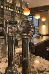 Chrome beer taps on a marble bar counter with globe pendant lights and a bottle-lined back bar