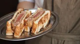 Breaded cutlet sandwiches sliced and stood upright on a metal serving tray