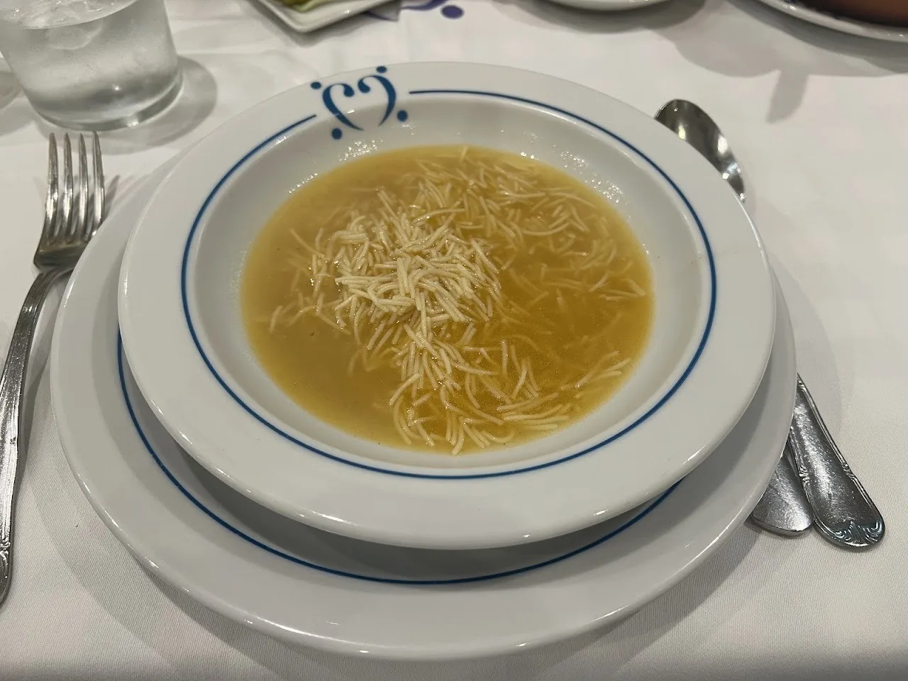 A bowl of clear noodle soup on a white plate with a blue rim